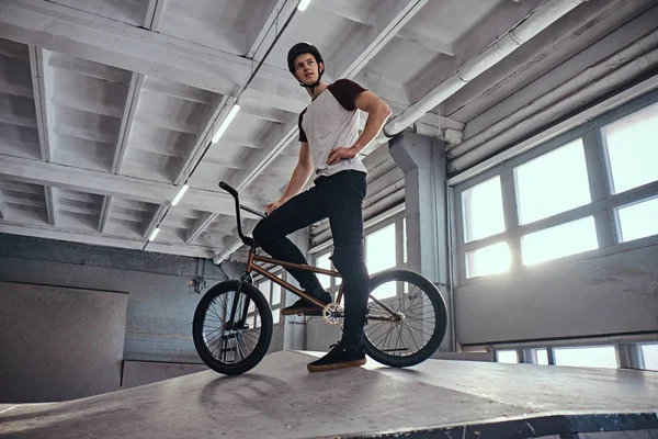 BMX гонщик стоїть зі своїм велосипедом готується стрибати в скейтпарку в приміщенні — стокове фото