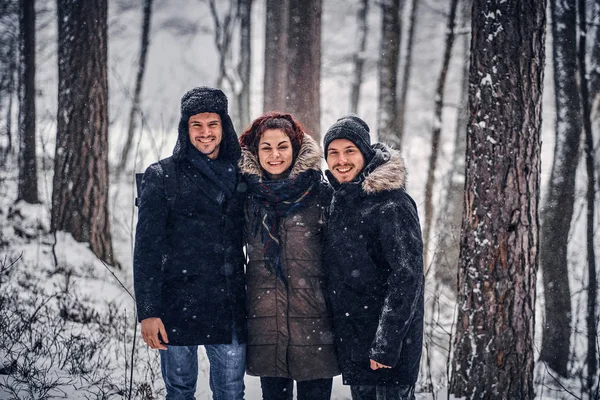 A group of happy friends stand next to each other and look at the camera in the midst of a snowy forest