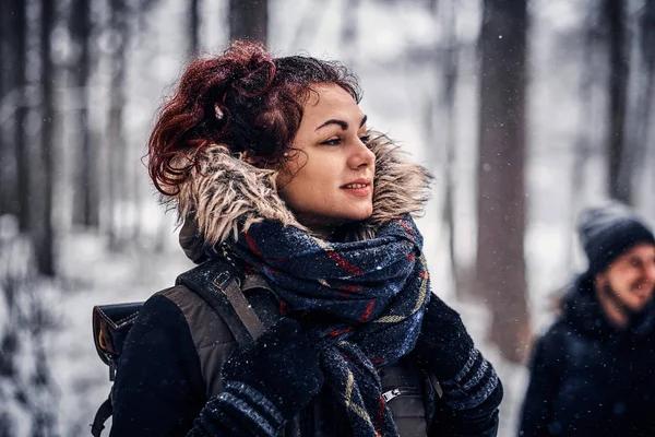 Gyönyörű vörös hajú lány egy séta a téli erdőben a barátaival hátizsák — Stock Fotó