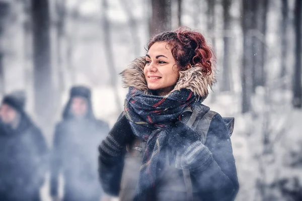 Menina ruiva bonita com uma mochila andando com seus amigos através de uma floresta de inverno — Fotografia de Stock