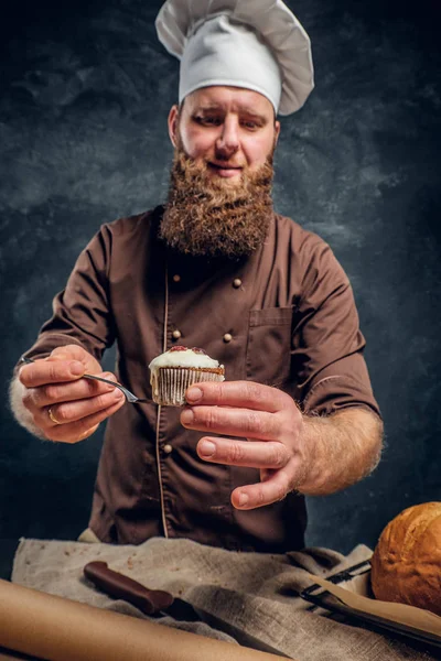 Baker vestindo um uniforme segurando um delicioso queque em um estúdio escuro . — Fotografia de Stock