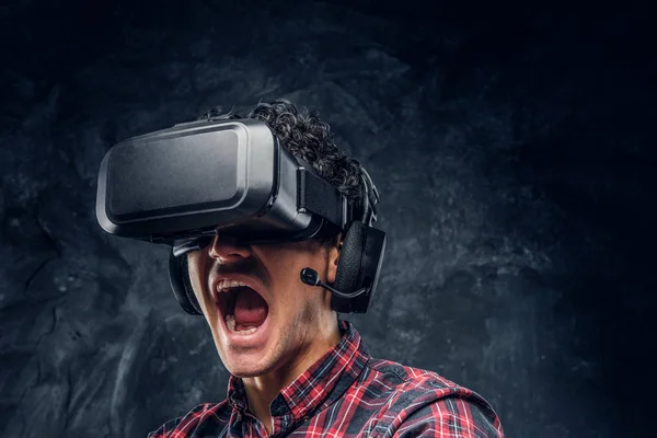 Portret van een jonge emotionele man met behulp van Vr headset en het afspelen van een video game in een studio tegen de achtergrond van de donkere muur — Stockfoto