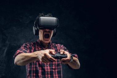 Duygusal adam VR kulaklık kullanarak ve joystick ile bilgisayar oyunu bir stüdyoda karanlık duvar arka plan karşı oynamak.