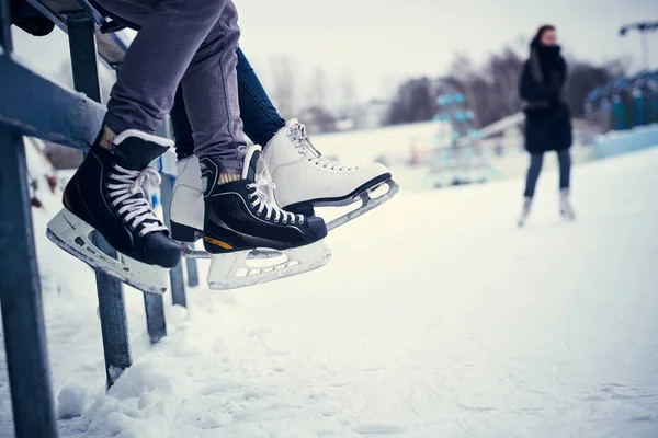 Couple wearing ice skates sitting on a guardrail
