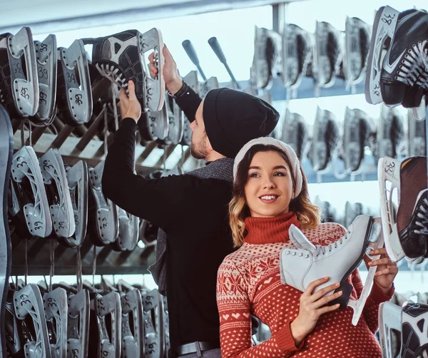 Junges Paar in warmer Kleidung, das in der Nähe des Gepäckträgers mit vielen Paar Schlittschuhe steht und seine Größe auswählt — Stockfoto