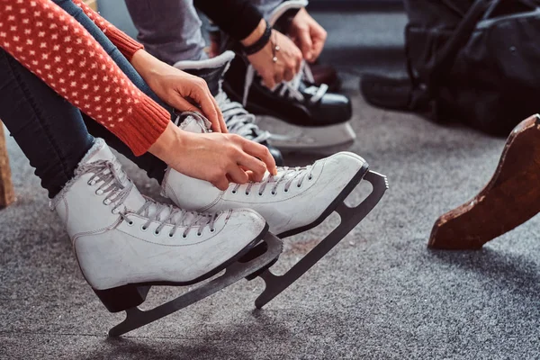 Молодая пара готовится к катанию на коньках. Крупным планом их руки завязывают шнурки хоккейных коньков в раздевалке — стоковое фото