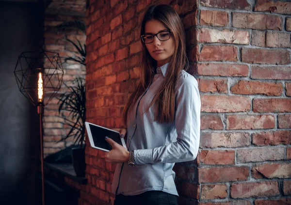 Akıllı kız tablet bir çatı katı iç odadaki bir tuğla duvara yaslanmış süre tutarak şık bir gömlek giymiş — Stok fotoğraf