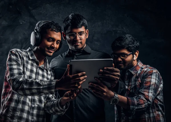 Τριών Ινδός φίλων βλέποντας κάτι διασκέδαση σε ένα tablet να στέκεται σε ένα σκοτεινό στούντιο — Φωτογραφία Αρχείου