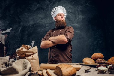 Lezzetli ekmek somunları, baget ekmek ve kek karanlık bir stüdyoda süslenmiş bir tablosunun yanındaki sakallı bir fırıncı giyen üniforma ayakta kollarını ile geçti