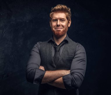 Şık giyinmiş Kızıl saçlı adam kollarını Studio bir karanlık dokulu duvara çarpı işareti ile poz