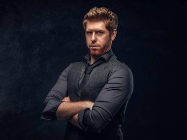 Şık giyinmiş Kızıl saçlı adam kollarını Studio bir karanlık dokulu duvara çarpı işareti ile poz
