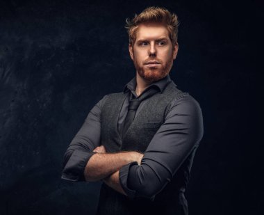 Şık giyinmiş Kızıl saçlı adam kollarını Studio bir karanlık dokulu duvara çarpı işareti ile poz