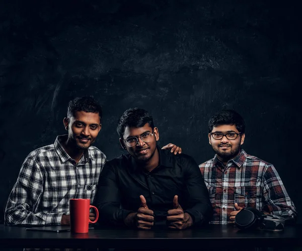 三个印度学生朋友坐在桌旁, 拥抱着, 看着相机 — 图库照片