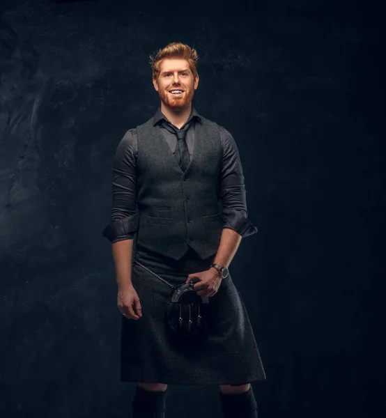 Redhead man dressed in an elegant vest with tie and kilt in studio against a dark textured wall — Stock Photo, Image