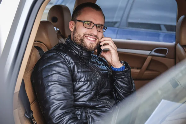 Hombre de negocios alegre sentado en un asiento trasero en el coche de lujo, hablando por teléfono —  Fotos de Stock