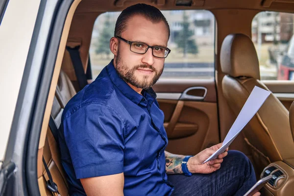 Vousatý podnikatel sedí na zadním sedadle v luxusních aut, držení důležitých dokumentů a při pohledu na fotoaparát — Stock fotografie