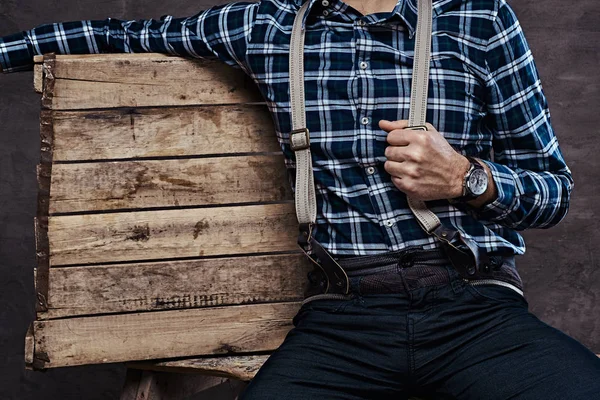 Cropped image. Old-fashioned man wearing a checkered shirt with suspenders sitting on a wooden scaffolding — Stock Photo, Image