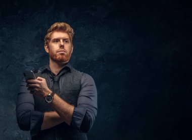 Formal giyim bir smartphone stüdyoda bir karanlık dokulu duvara tutan yakışıklı Kızıl saçlı adam