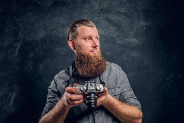 Bir şık saç ve sakal bir fotoğraf makinesi tutan bir gri gömlek giymiş bir adam.