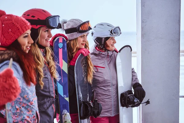 Πορτραίτο των γυναικών φίλους στο σπορ χειμερινά ρούχα κρατώντας σνόουμπορντ και σκι στέκεται μαζί κοντά στις ακτές της θάλασσας χιονισμένο — Φωτογραφία Αρχείου