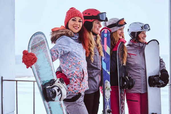 Retrato de una mujer amiga en ropa deportiva de invierno sosteniendo tablas de snowboard y esquís de pie junto a la costa nevada del mar —  Fotos de Stock