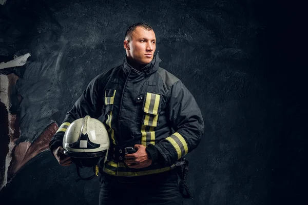 Brutal bombero mira hacia los lados y sostiene un casco en su mano — Foto de Stock