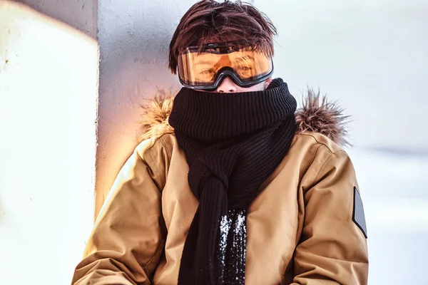 Μια εφηβική snowboarder ντυμένος με snowsuit και προστατευτικά γυαλιά, κάθεται στο κιγκλίδωμα κοντά στην παραλία χιονισμένο — Φωτογραφία Αρχείου