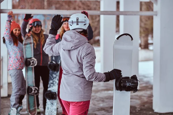 Mujer snowboarder sosteniendo una tabla vuelta para saludar a los amigos en la estación de esquí de invierno —  Fotos de Stock