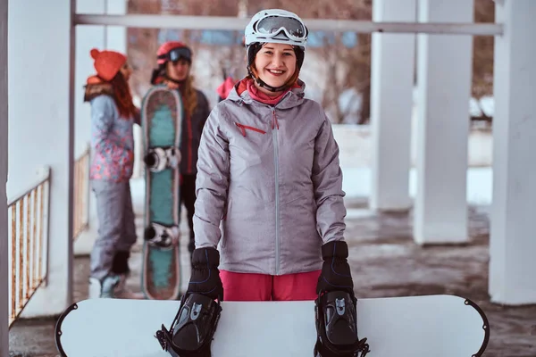 Femeia zâmbitoare purtând îmbrăcăminte sport de iarnă pozând cu un snowboard în stațiunea de schi de iarnă — Fotografie, imagine de stoc