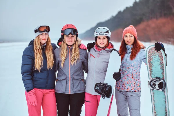 Γυναίκες φίλους σε σπορ χειμερινά ρούχα με σνόουμπορντ και σκι στέκεται μαζί σε μια αγκαλιά και εξετάζοντας τη φωτογραφική μηχανή — Φωτογραφία Αρχείου