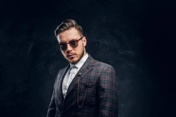 Elegantemente vestido joven en gafas de sol contra una pared de textura oscura — Foto de Stock