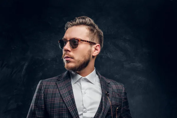 Elegantemente vestido joven en gafas de sol contra una pared de textura oscura — Foto de Stock