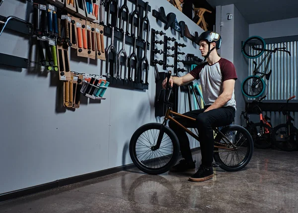 Jovem sentado em sua bicicleta ao lado de um estande com peças BMX em uma loja de bicicletas — Fotografia de Stock
