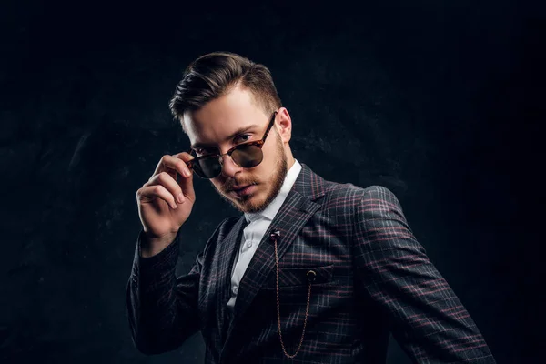 Elegantemente vestido joven en gafas de sol contra una pared de textura oscura — Foto de Stock