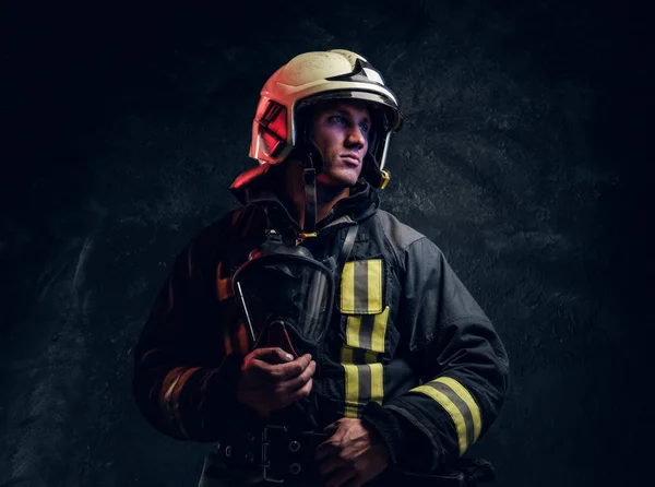 Bombeiro brutal em uniforme e capacete de segurança segurando uma máscara de oxigênio e olhando para o lado com um olhar confiante . — Fotografia de Stock