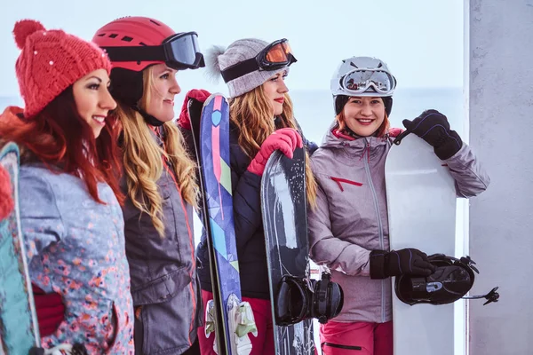 Retrato de mulheres amigas em esportes roupas de inverno segurando snowboards e esquis juntos perto da costa do mar nevado — Fotografia de Stock