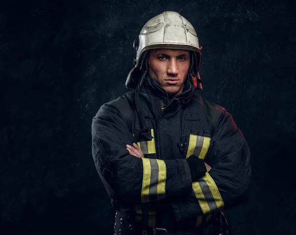 Bombero brutal en uniforme posando para la cámara de pie con los brazos cruzados y mirada confiada . — Foto de Stock