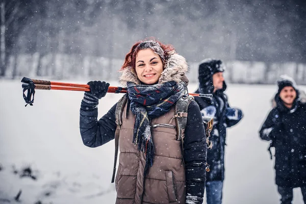 Piękne redhead dziewczyna z plecakiem chodzenie z kolegami przez las zima — Zdjęcie stockowe