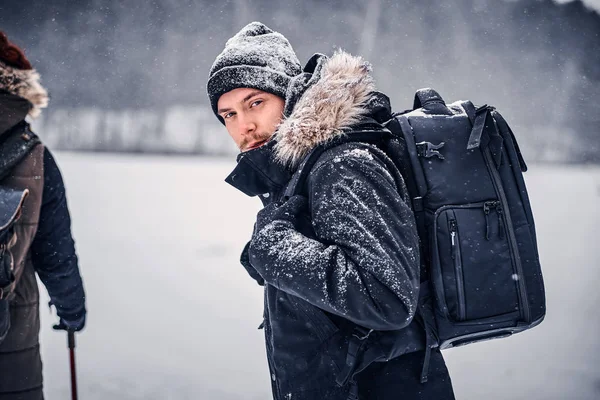 Porträtt av en ung hiker kille med en ryggsäck som promenader med sin flickvän genom en vinter skog — Stockfoto