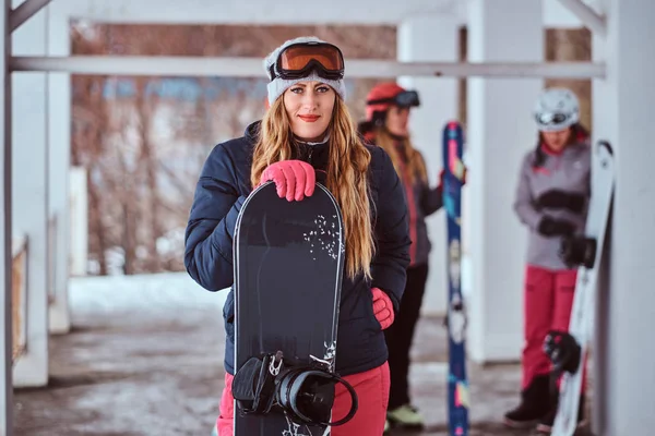 Mujer noruega con ropa de abrigo y gafas posando con una tabla de snowboard en la estación de esquí de invierno —  Fotos de Stock