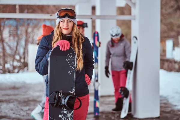 Mujer noruega con ropa de abrigo y gafas posando con una tabla de snowboard en la estación de esquí de invierno —  Fotos de Stock