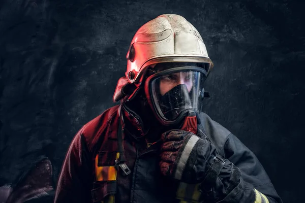 Portrait of a firefighter in safety helmet and an oxygen mask in dark studio — Stock Photo, Image