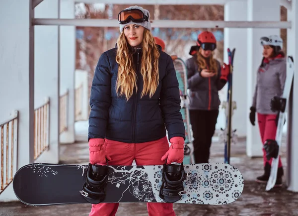 Mujer noruega con ropa de abrigo y gafas posando con una tabla de snowboard en la estación de esquí de invierno —  Fotos de Stock