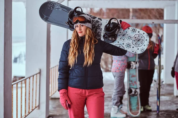 Mujer noruega con ropa de abrigo y gafas posando con una tabla de snowboard en la estación de esquí de invierno —  Fotos de Stock