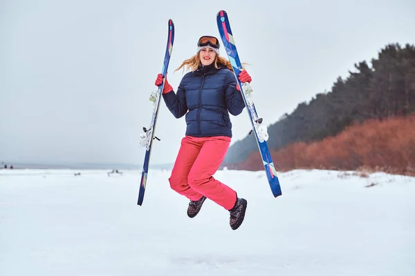 Munter kvinde iført opvarmning sportstøj hoppe med ski på en snedækket strand - Stock-foto