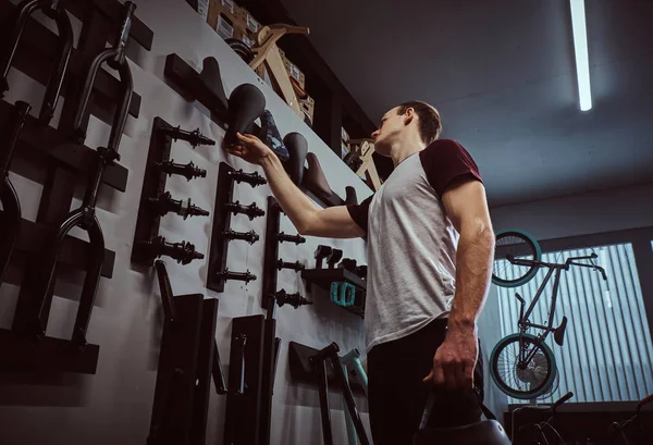 Teenage BMX rider holding a protective helmet and choosing parts for his bike shop in bicycle shop — стоковое фото