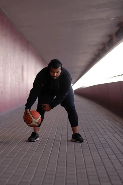 Afro-americano vestindo um capuz preto jogando basquete em uma calçada ponte — Fotografia de Stock