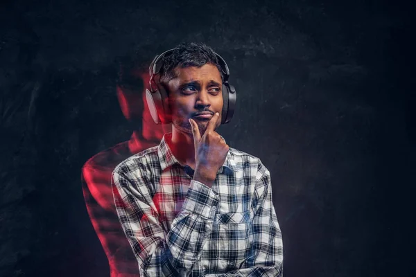 Portret van een knappe Indiase man dragen een geruite shirt luistert naar muziek in draadloze hoofdtelefoons met doordachte look — Stockfoto