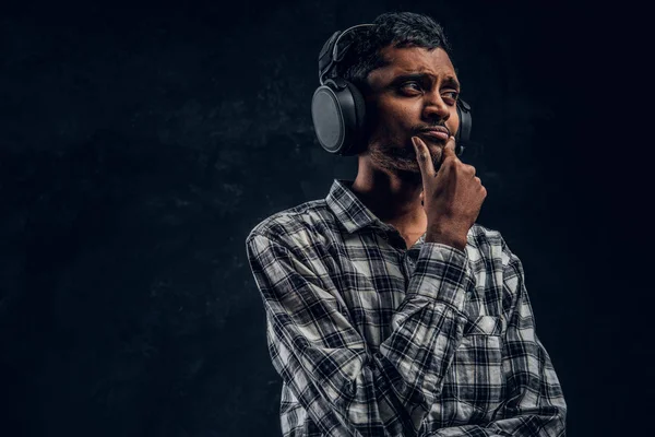 Πορτρέτο του ένα όμορφο ινδική άνθρωπος φορώντας ένα καρό πουκάμισο που ακούει μουσική σε ασύρματα ακουστικά με το στοχαστικό βλέμμα — Φωτογραφία Αρχείου