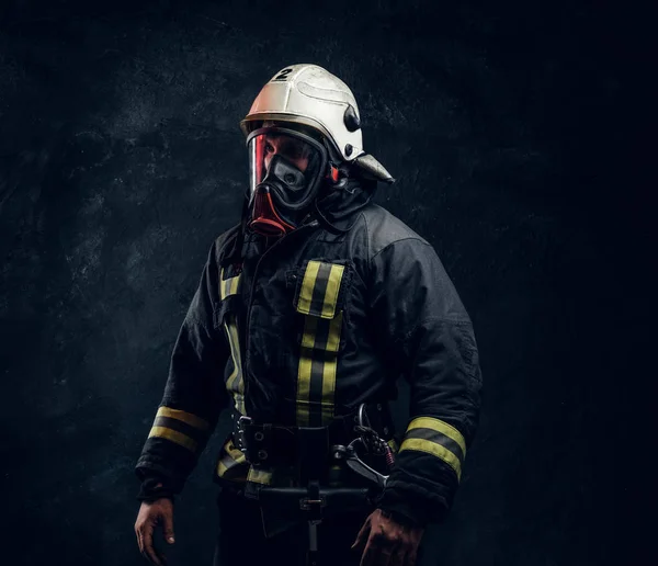 Retrato de um homem em equipamento de bombeiro completo posando em um estúdio escuro — Fotografia de Stock
